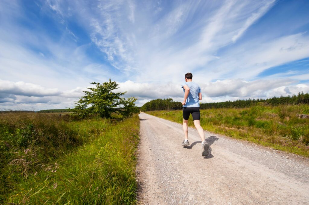 A person running on a dirt path between two green grass fields.